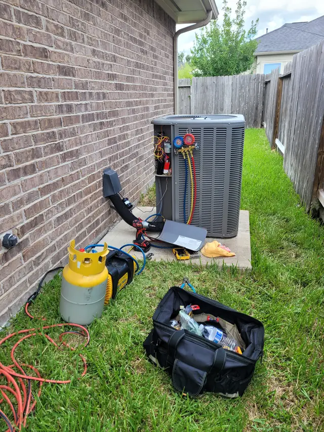 Condenser with its service panel off, manifold gauges connected and a recovery tank beside it