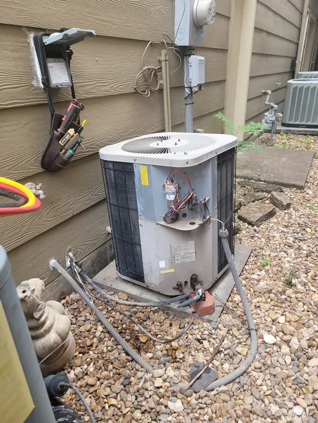 Condenser access panel open with capacitor and contactor wiring exposed and a meter in the tool pouch